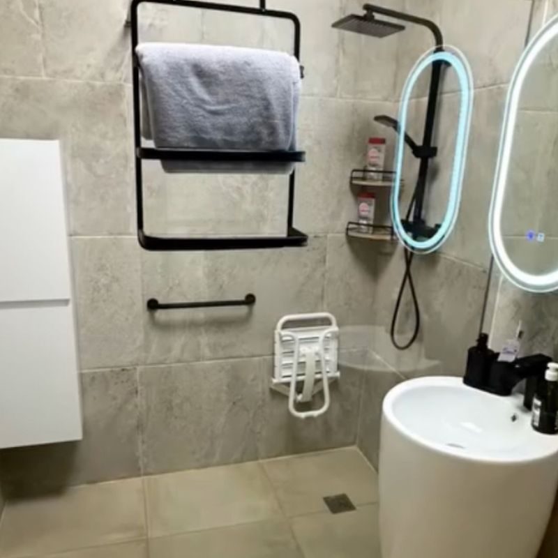 Salle de bain moderne rénovée avec carrelage gris, vasque blanche, miroir lumineux, étagère murale noire et accessoires de