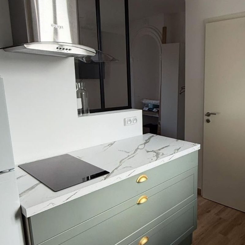 Cuisine moderne avec îlot central couleur menthe, plan de travail en marbre blanc, rangements dorés et électroménager intégré