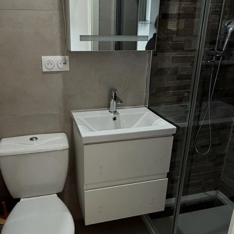 Salle de bain moderne avec toilettes blanches, meuble vasque deux tiroirs, miroir, miroir mural et douche encadrée